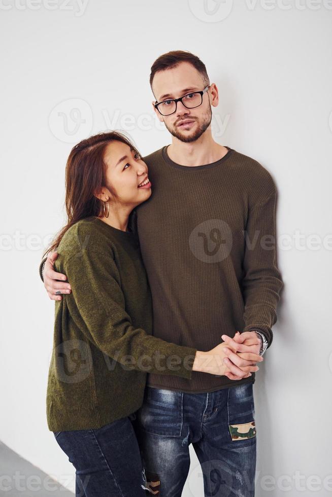 heureux couple multiethnique en vêtements décontractés est ensemble à l'intérieur dans le studio. mec caucasien avec petite amie asiatique photo