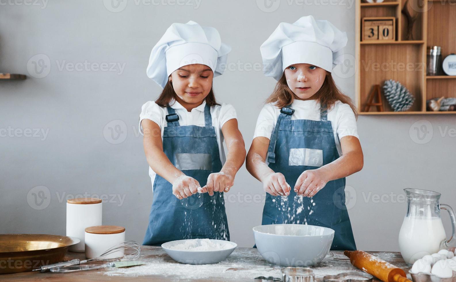 deux petites filles en uniforme de chef bleu travaillant avec de la farine dans la cuisine photo