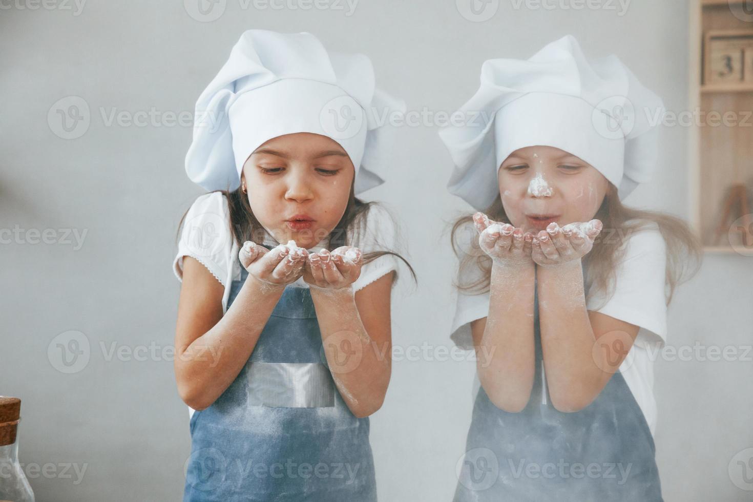 deux petites filles en uniforme de chef bleu soufflent la farine des mains sur la cuisine photo