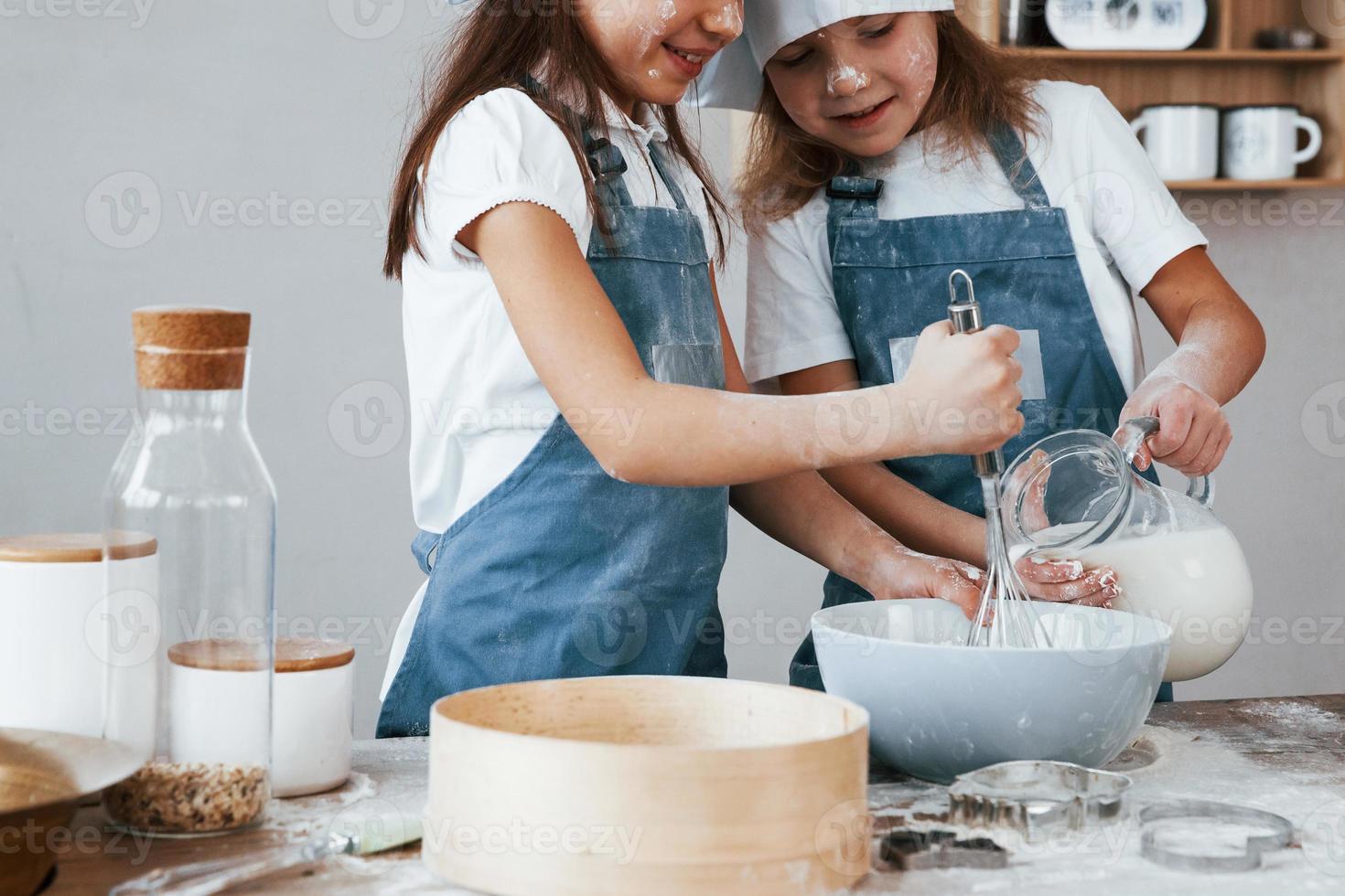 deux petites filles en uniforme de chef bleu mélangeant de la farine avec des œufs dans une assiette sur la cuisine photo