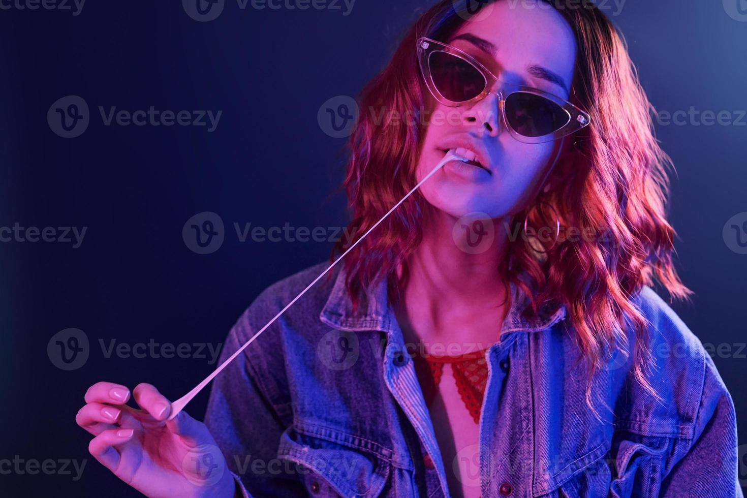 portrait de jeune fille à lunettes avec bubble-gum en néon rouge et bleu en studio photo