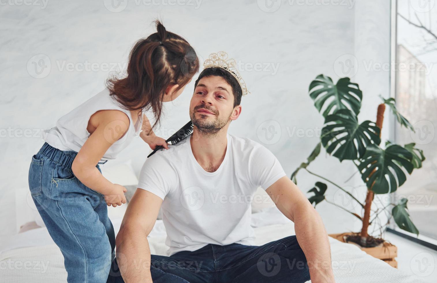 petite fille portant une couronne sur la tête du père. s'amuser ensemble à la maison photo