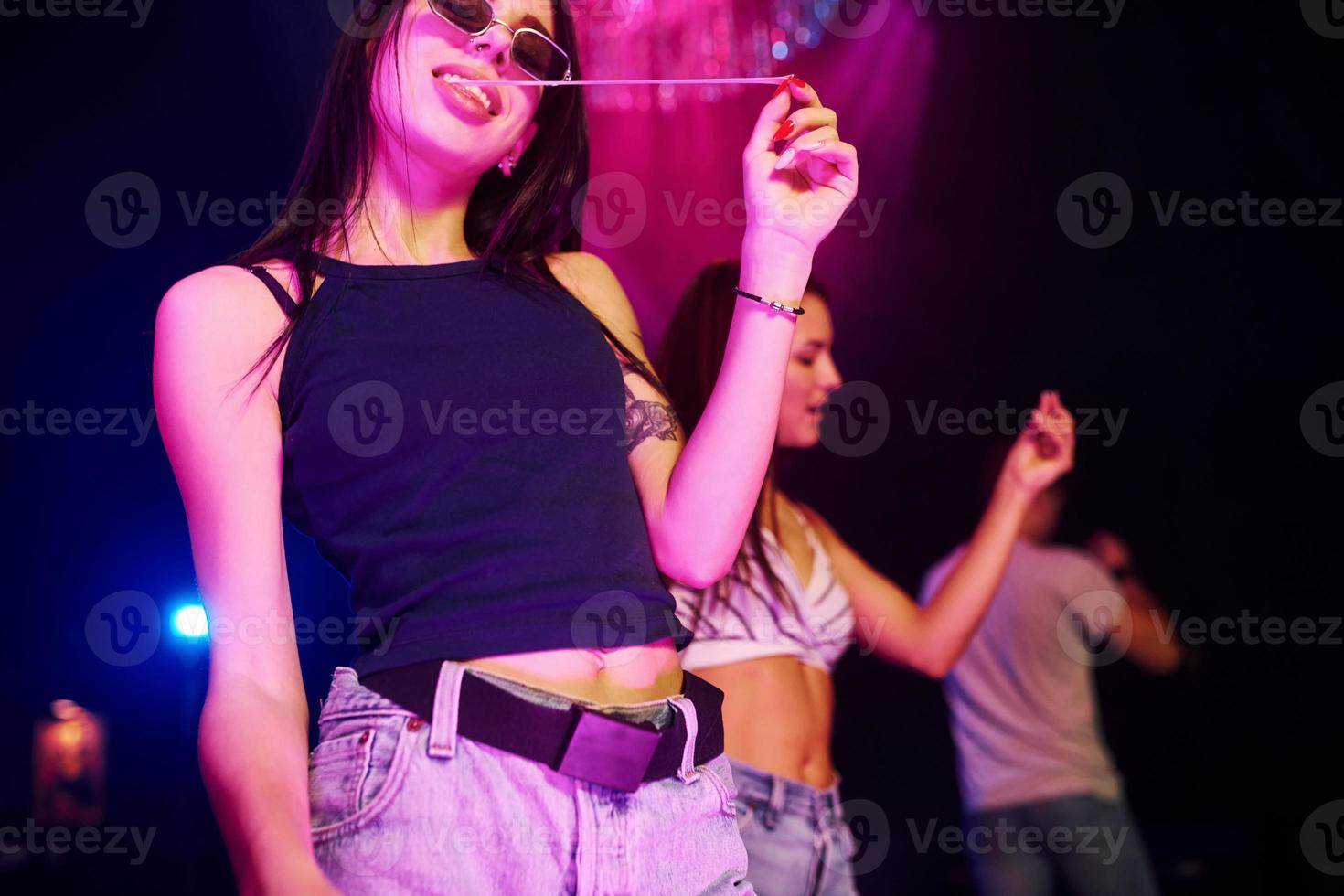 portrait de jeune fille à lunettes de soleil qui mâche de la gomme. les jeunes s'amusent dans une boîte de nuit avec des lumières laser colorées photo