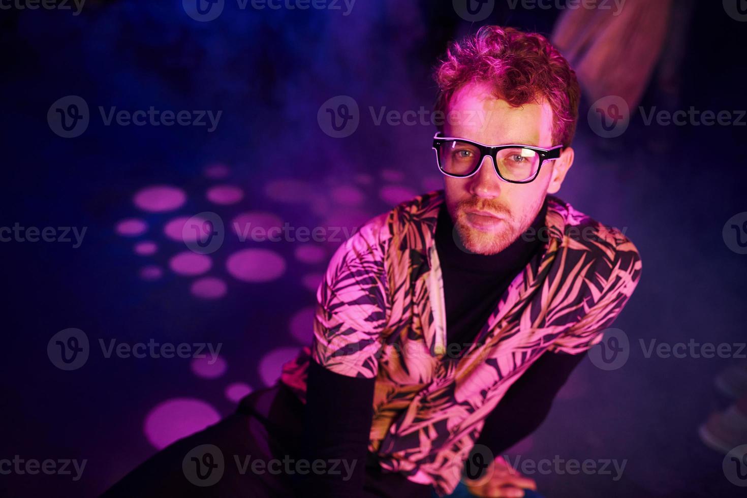 un jeune homme à lunettes s'amuse à l'intérieur d'une boîte de nuit avec des éclairages roses photo