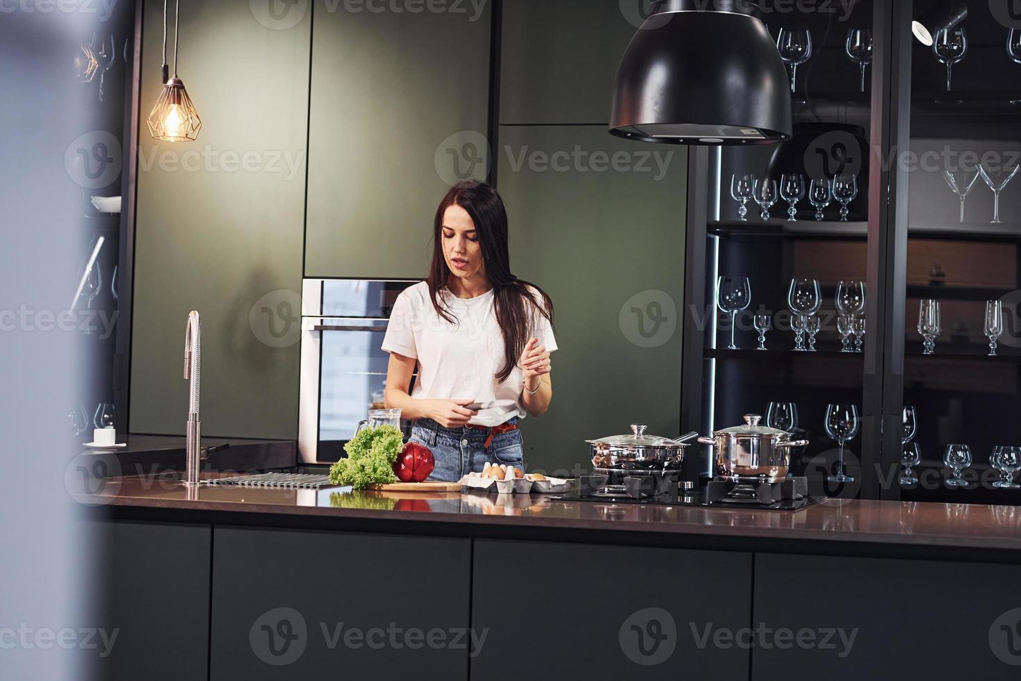 légumes et lait sur table. préparer la nourriture. jeune belle brune en vêtements décontractés à l'intérieur dans la cuisine pendant la journée photo