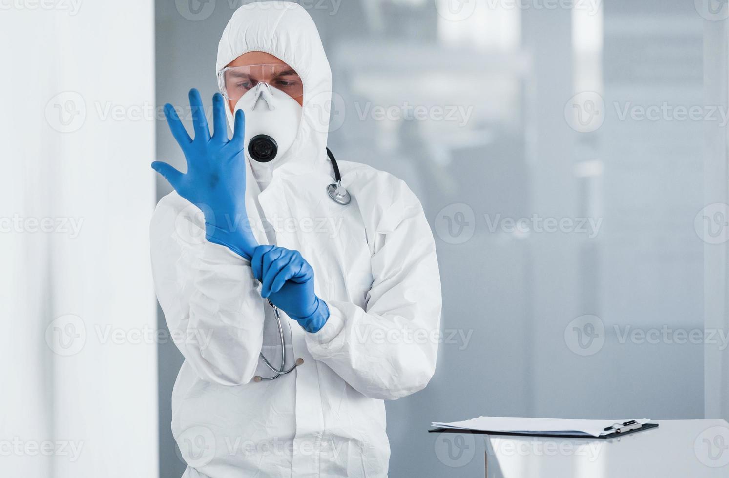 homme médecin scientifique en blouse de laboratoire, lunettes défensives et masque portant des gants bleus photo