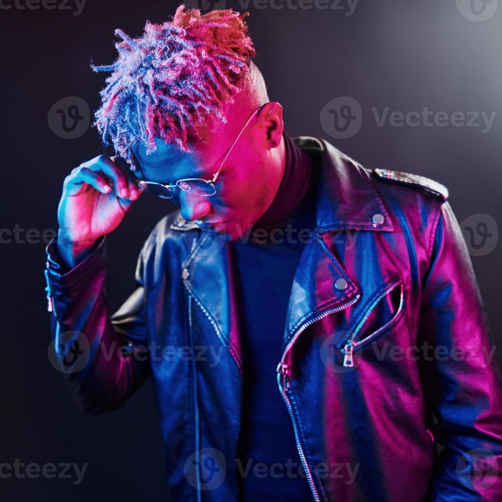 éclairage néon futuriste. jeune homme afro-américain à lunettes debout en studio photo