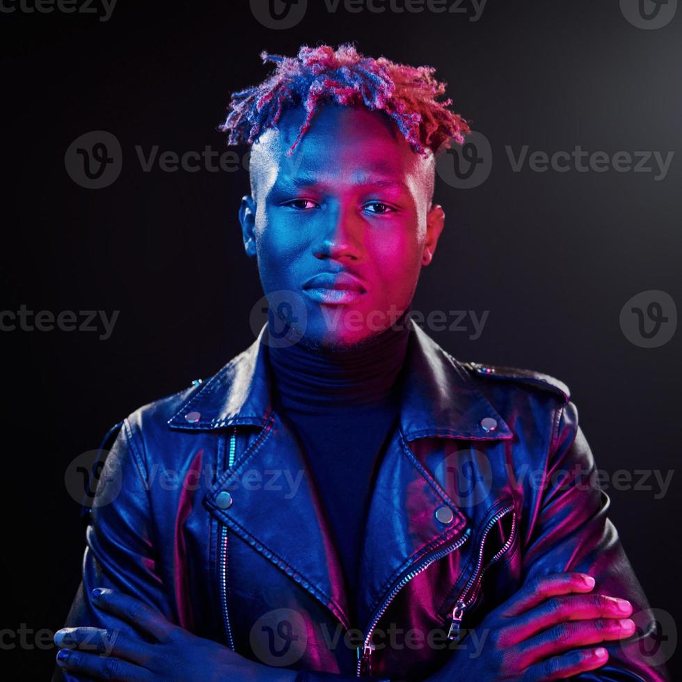 éclairage néon futuriste. jeune homme afro-américain debout en studio avec les bras croisés photo