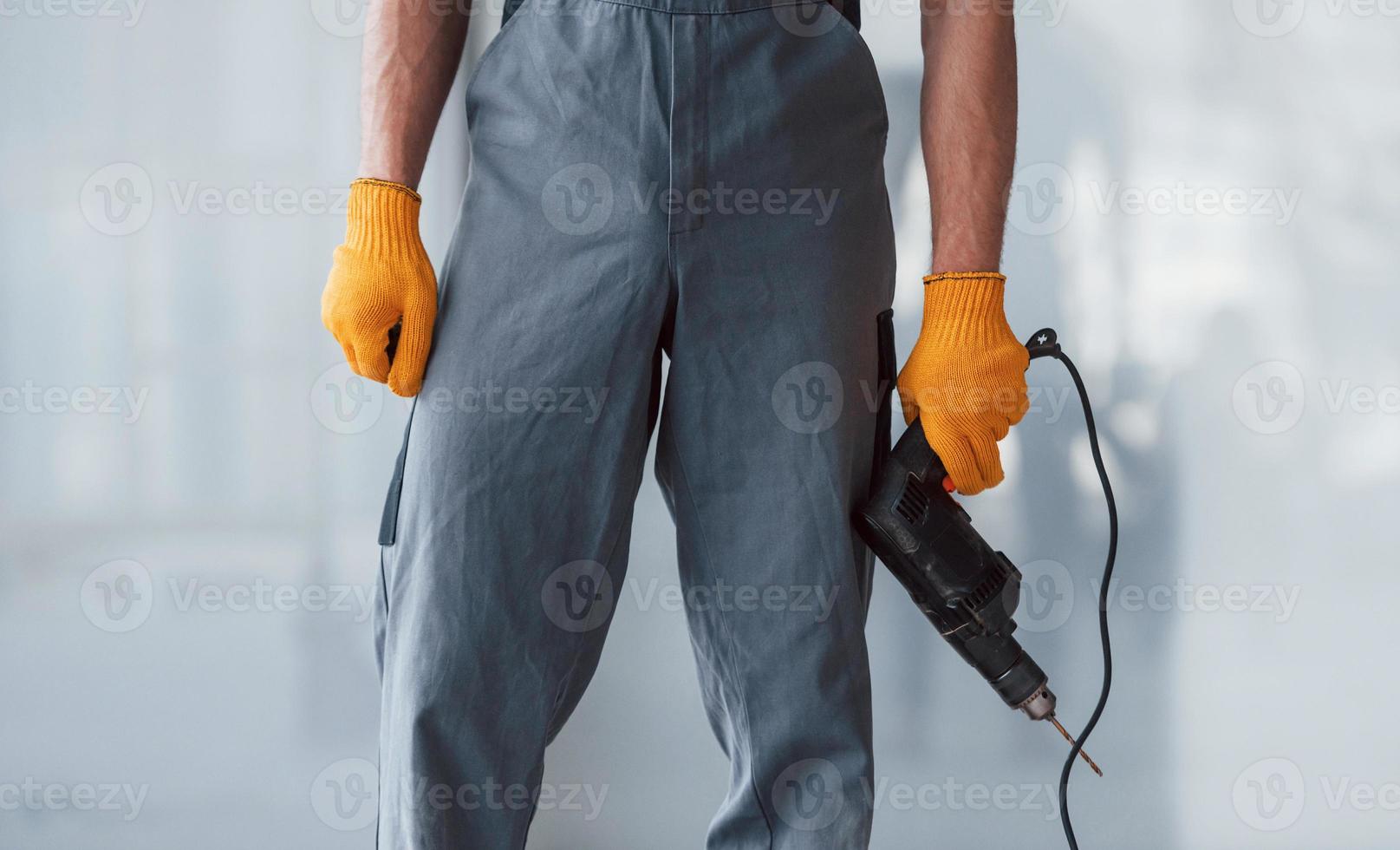 vue rapprochée de l'homme en uniforme gris avec une perceuse à la main à l'intérieur dans un grand bureau moderne pendant la journée photo