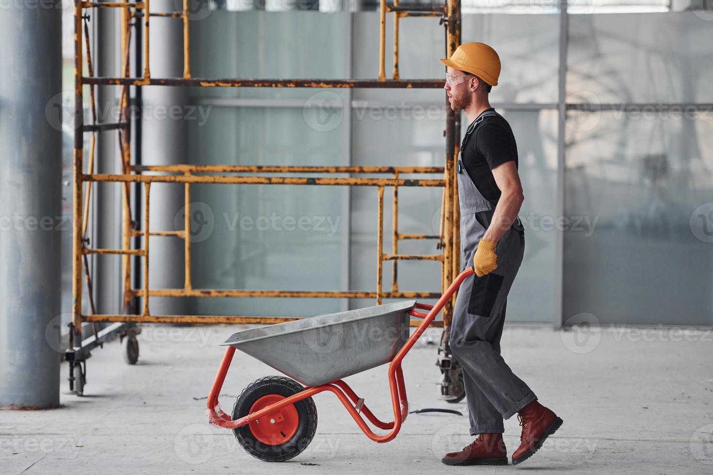 marche avec des brouettes. homme en uniforme gris travaille à l'intérieur dans un grand bureau moderne pendant la journée photo