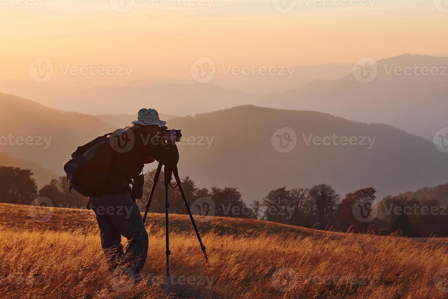 photographe masculin debout et travaillant dans un paysage majestueux d'arbres d'automne et de montagnes à l'horizon photo