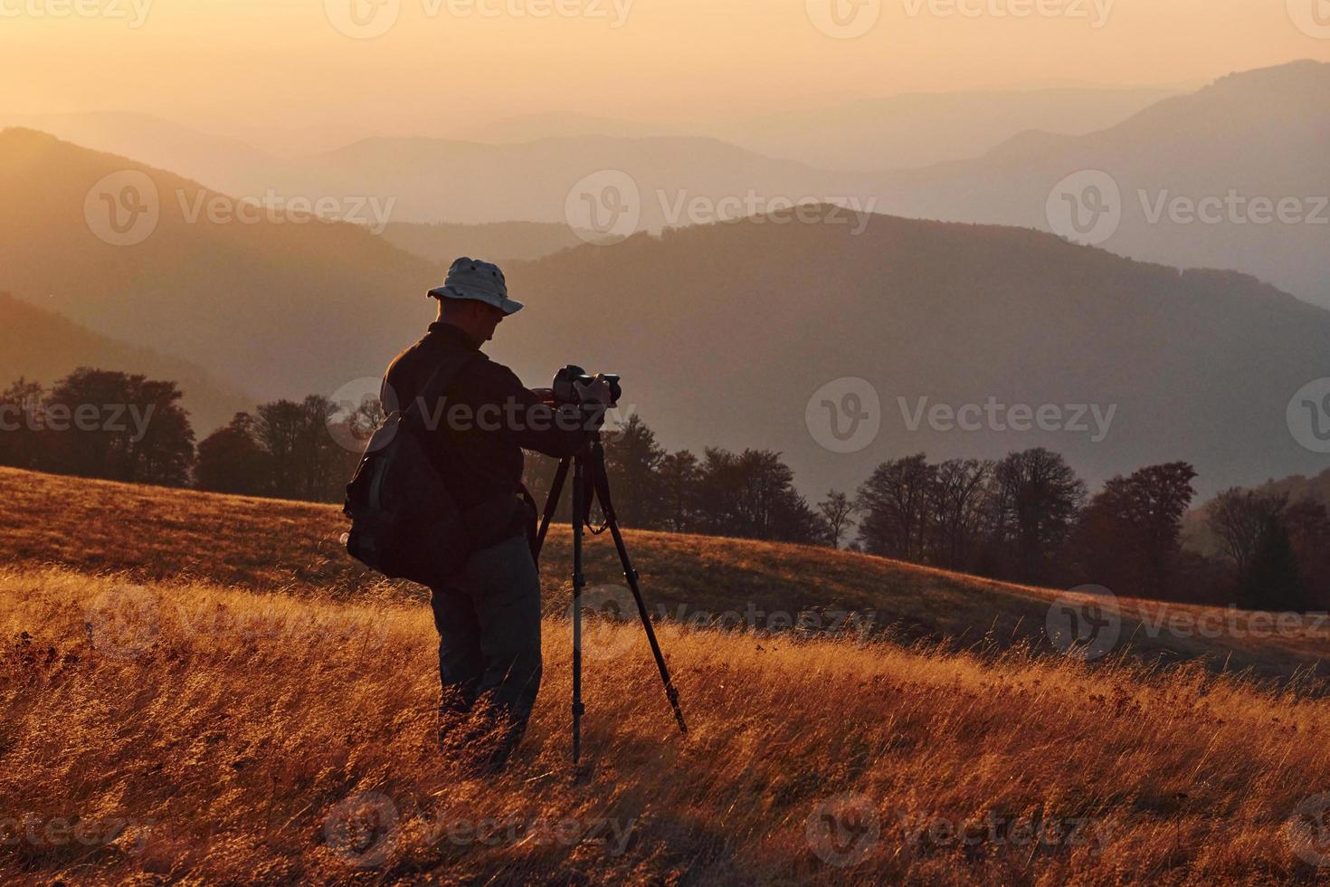 photographe masculin debout et travaillant dans un paysage majestueux d'arbres d'automne et de montagnes à l'horizon photo