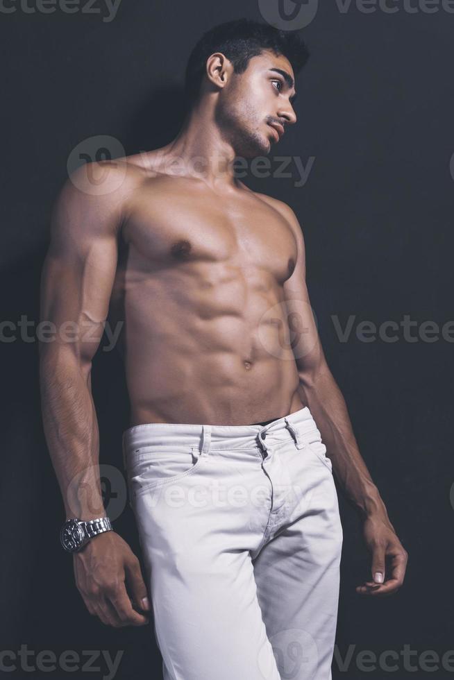 beau modèle masculin arabe avec un corps parfait qui pose en studio. portrait d'un modèle masculin athlétique posant sur fond sombre dans le studio. notion de mode. photo