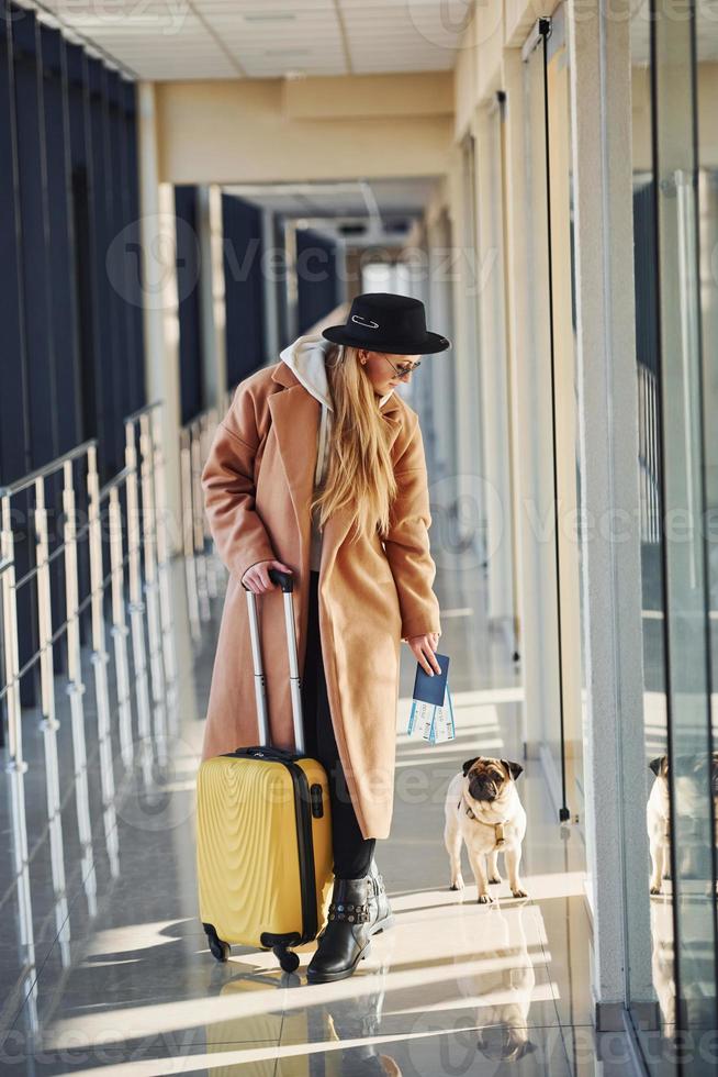 jeune passagère en vêtements chauds avec billets, son chien et ses bagages dans le hall de l'aéroport photo