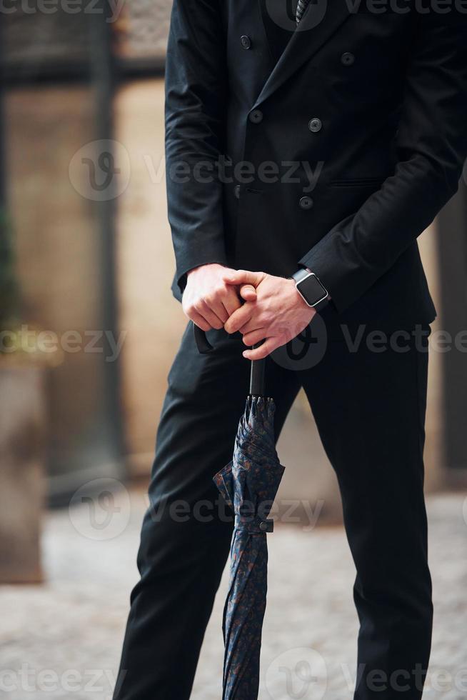 vue rapprochée. tenant un parapluie. jeune homme élégant dans des vêtements chics formels à l'extérieur de la ville photo