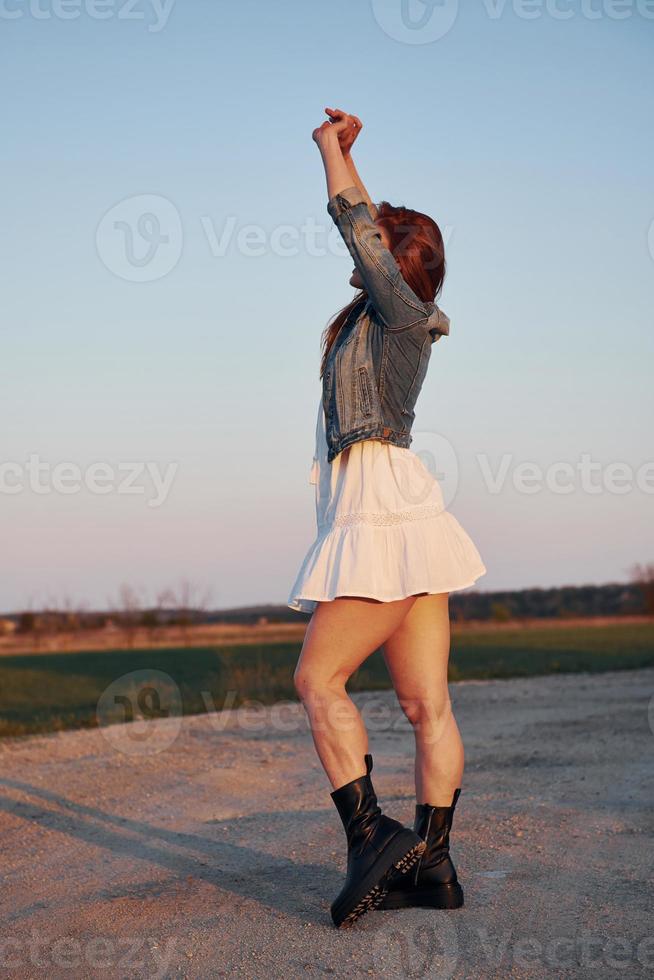 femme rousse en jupe debout et posant pour un appareil photo sur la route le soir