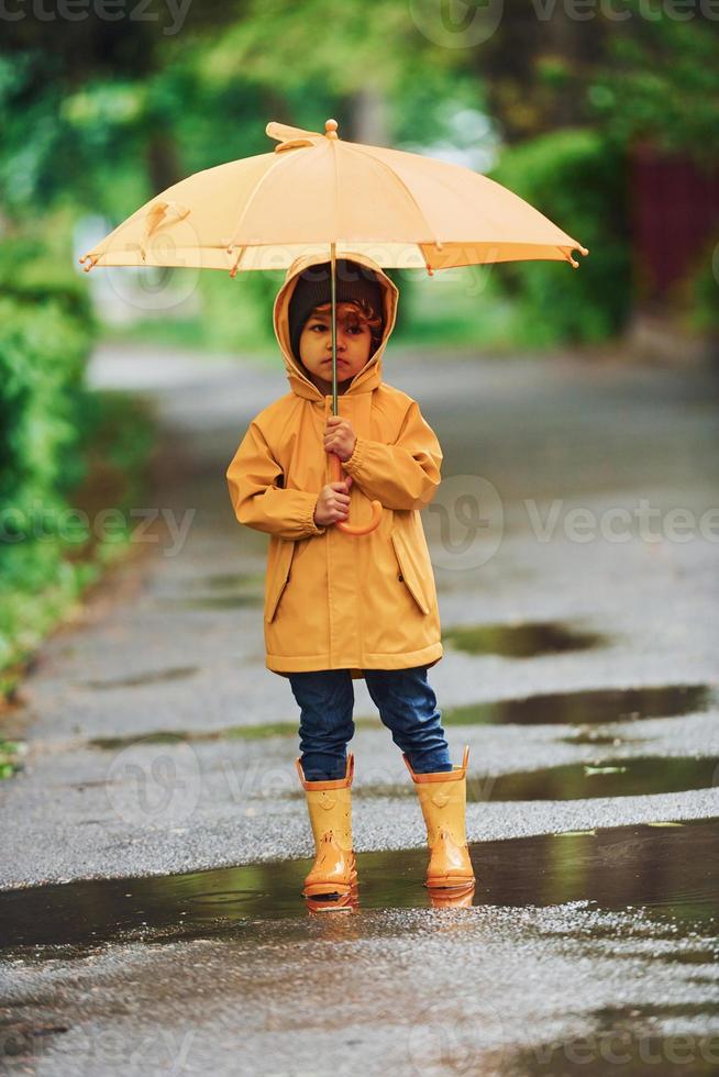 Enfant En Imperméable Jaune Avec Grand Parapluie Jaune Dans Les Mains Sur  Fond De Parc D'automne. Portrait D'un Garçon Marchant. Banque D'Images et  Photos Libres De Droits. Image 193353206