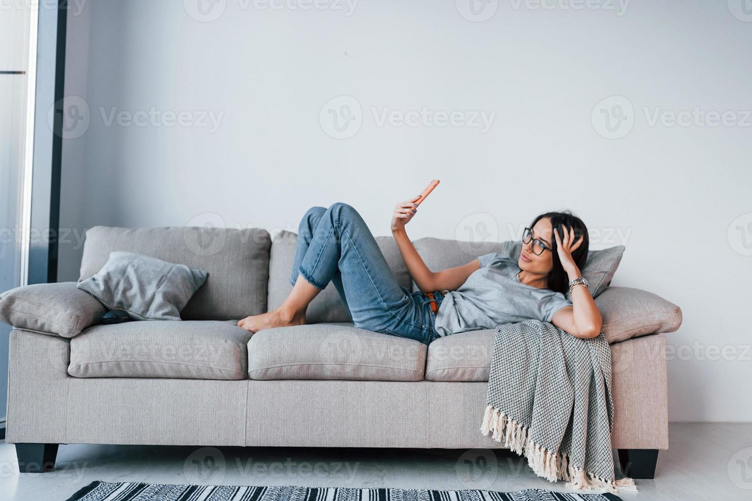 belle jeune femme en tenue décontractée allongée seule à la maison avec un smartphone dans les mains photo