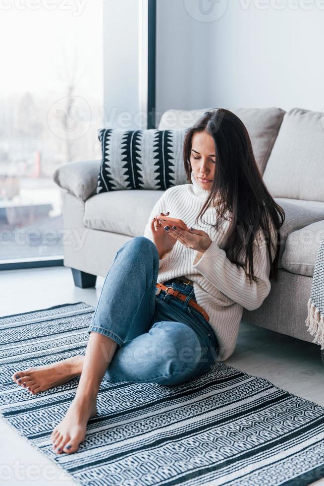 belle jeune femme en tenue décontractée assise à la maison seule avec un téléphone dans les mains photo