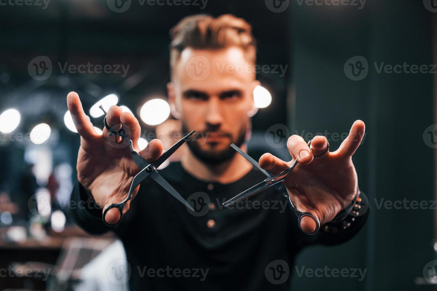 jeune homme barbu debout dans un salon de coiffure et tenant des ciseaux photo