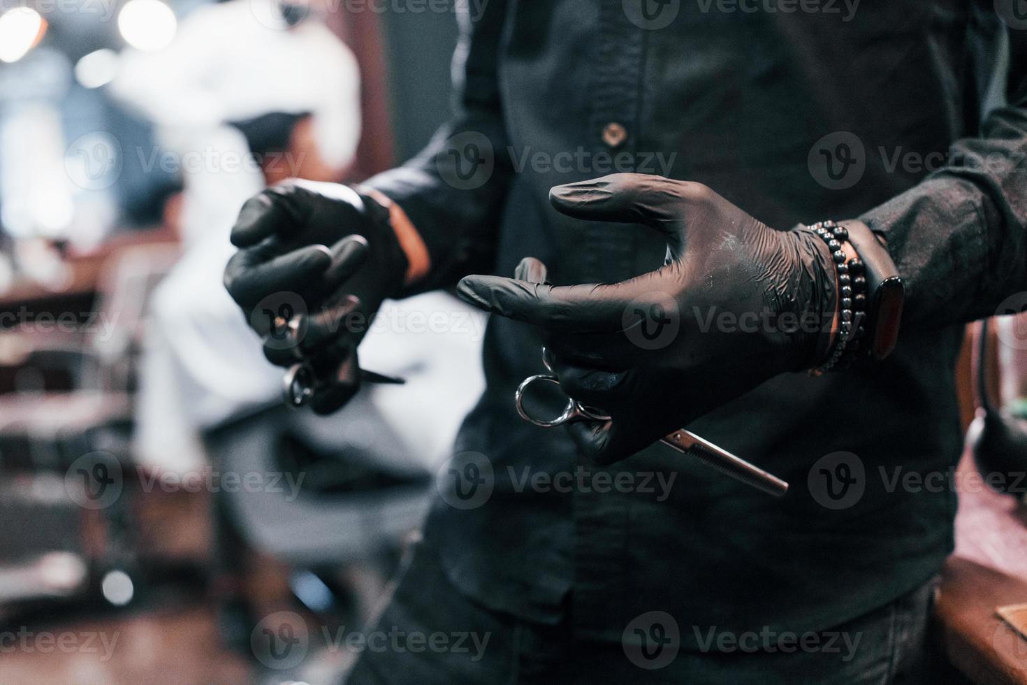 vue rapprochée d'un gars en vêtements noirs qui se tient à l'intérieur dans un salon de coiffure et tient des ciseaux photo