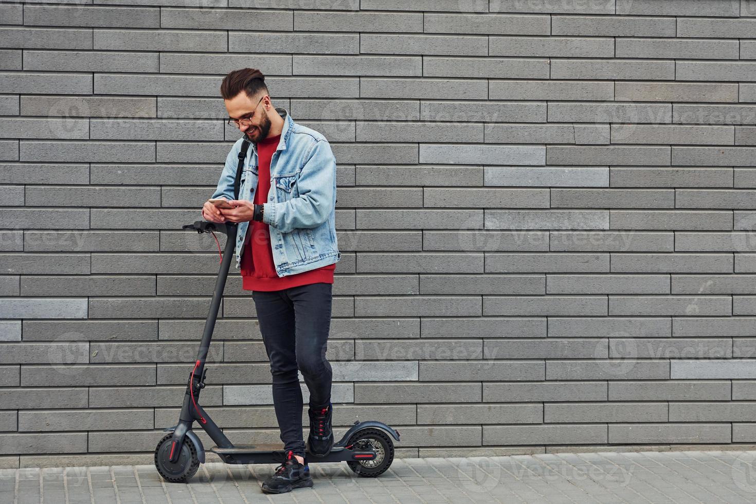 beau jeune homme en vêtements décontractés debout avec un scooter électrique à l'extérieur pendant la journée ensoleillée photo