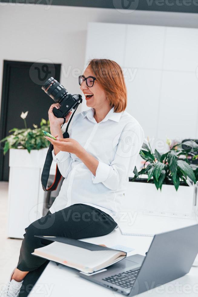 femme en vêtements formels et avec caméra assise au bureau photo