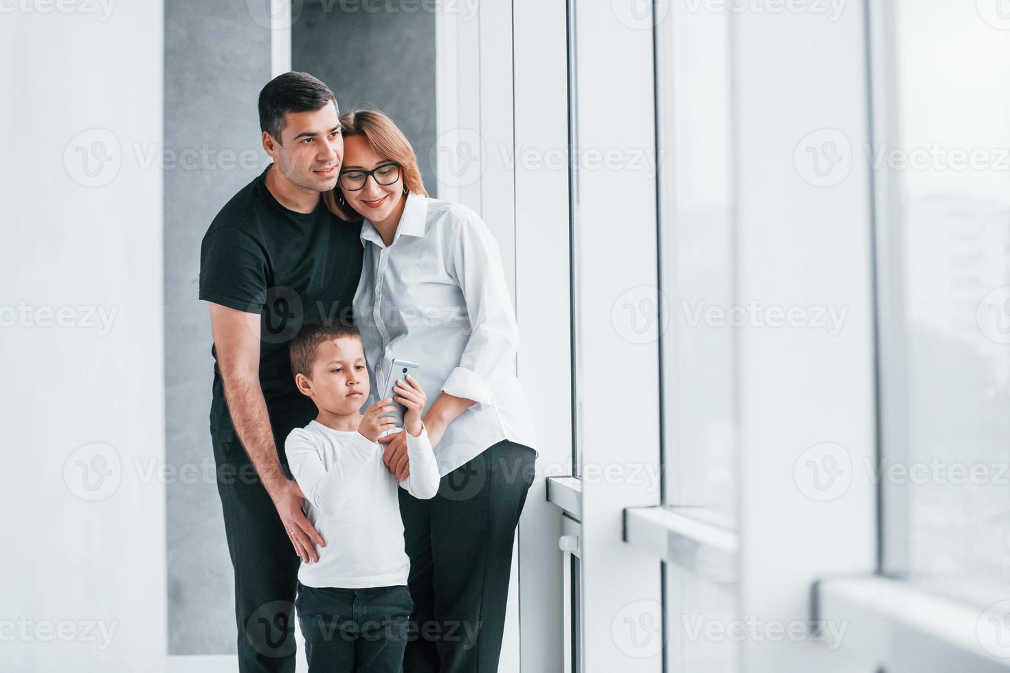 femme en vêtements formels et avec caméra à la main debout à l'intérieur d'une pièce vide avec homme et petit garçon photo