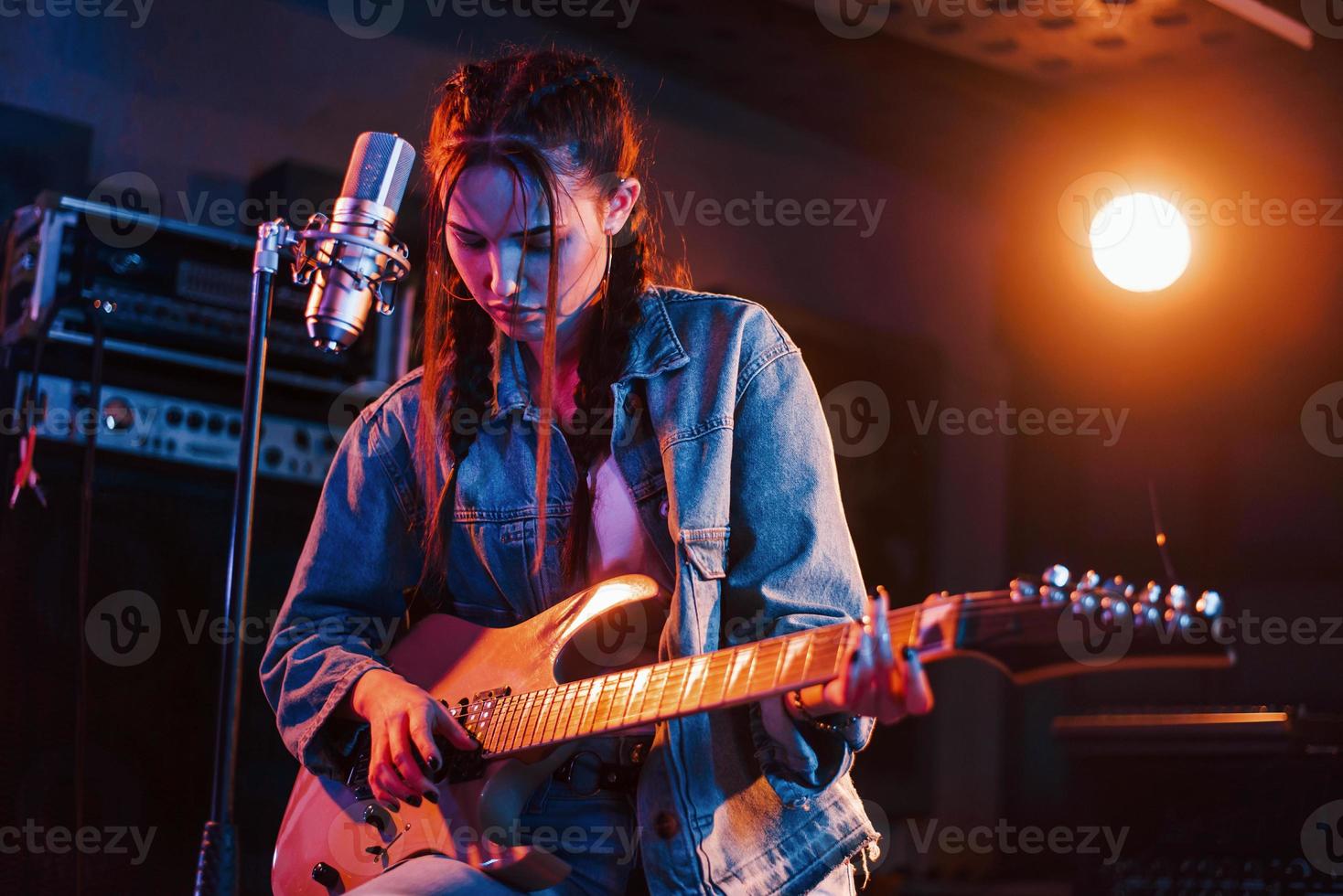 jeune belle interprète féminine avec guitare chantant et répétant dans un studio d'enregistrement photo