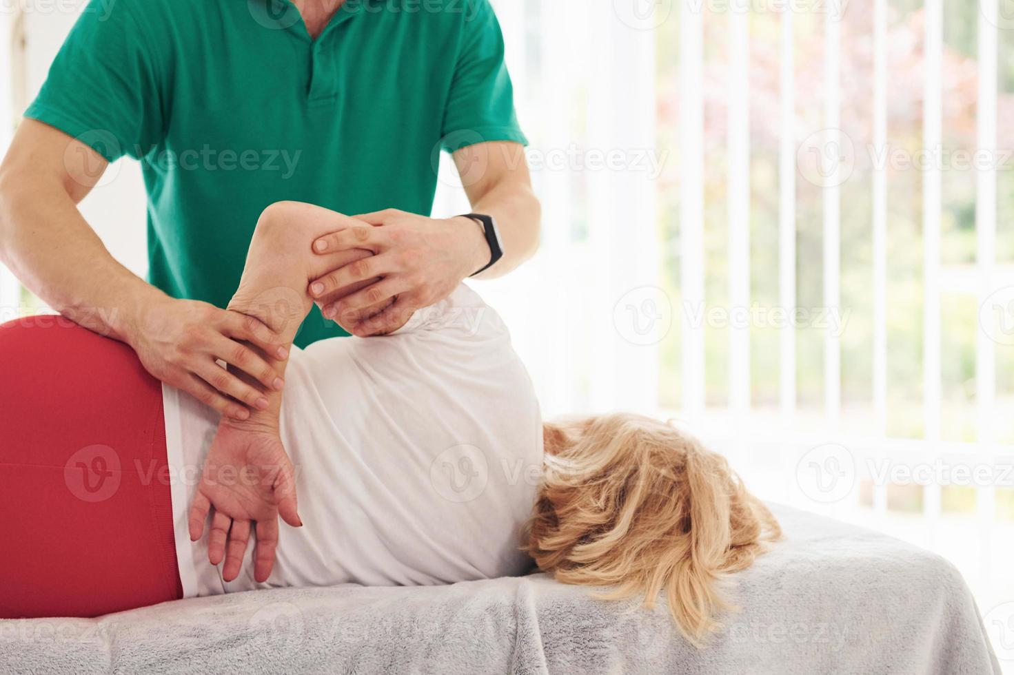 une femme plus âgée a une visite à la clinique, allongée et en rééducation. instructeur masculin l'aidant photo