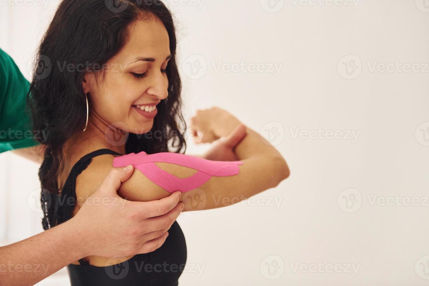 travailler avec du ruban adhésif. une jeune femme avec un type de corps de forme physique a une visite dans une clinique de réadaptation. instructeur l'aidant photo