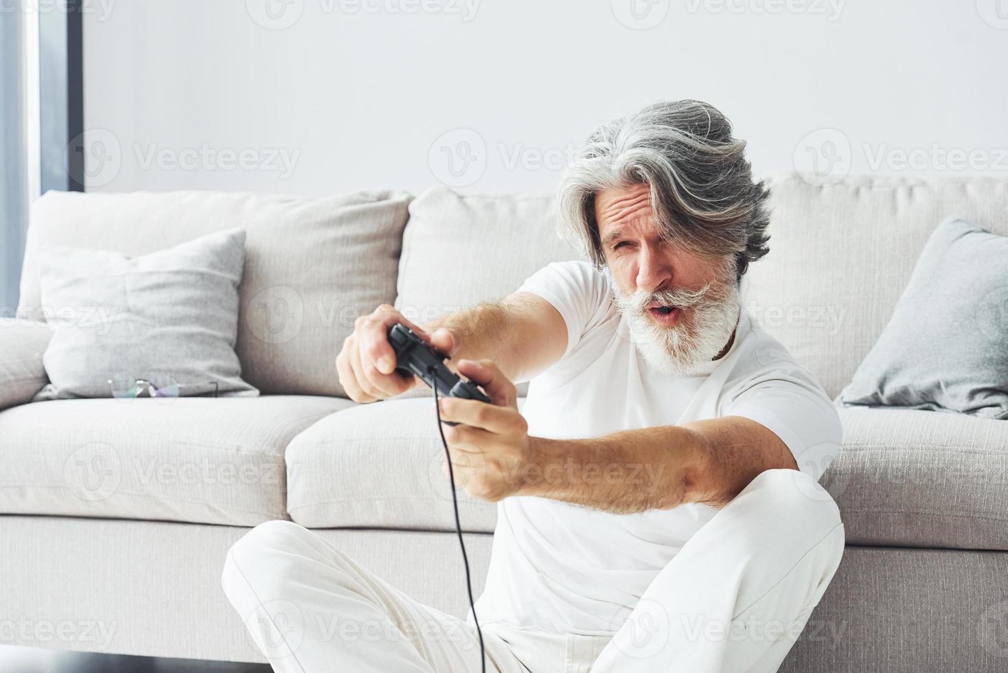 joue au jeu vidéo en utilisant le contrôleur. homme moderne et élégant aux cheveux gris et à la barbe à l'intérieur photo