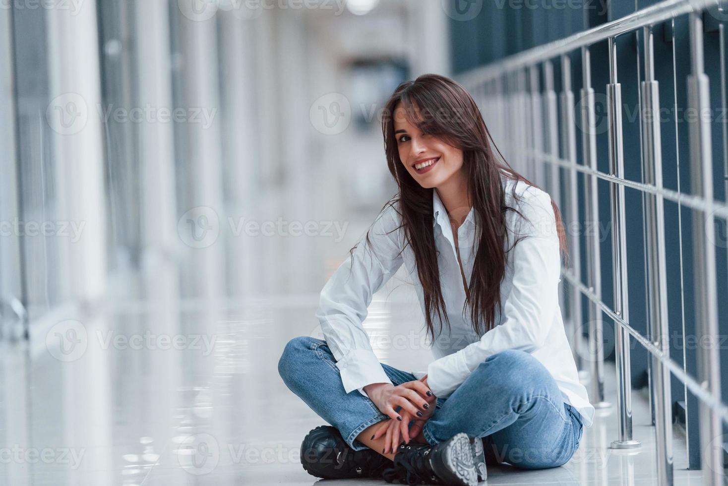 brune en chemise blanche est assise à l'intérieur dans un aéroport ou un couloir moderne pendant la journée photo