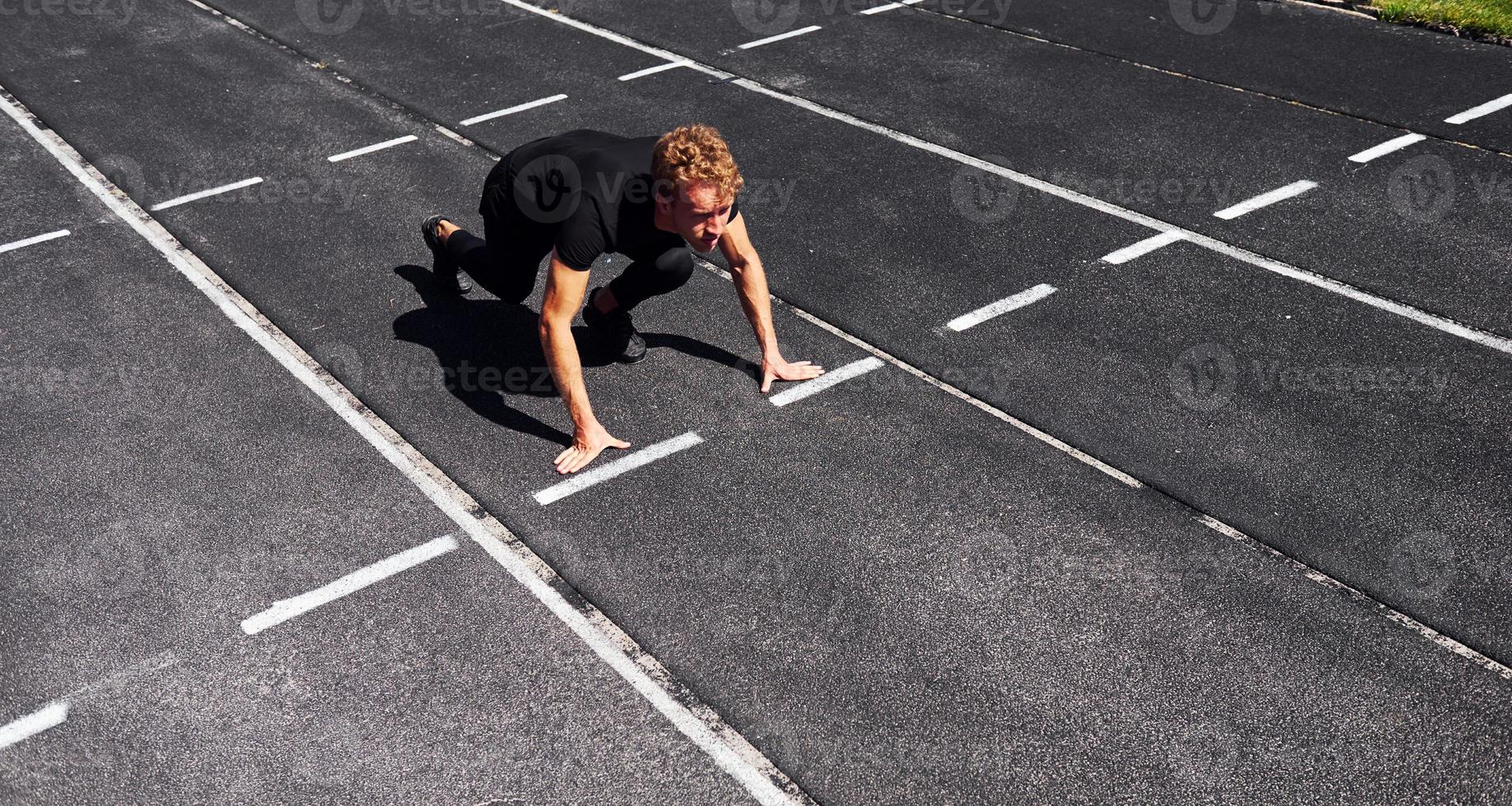 le coureur est en position de départ sur la piste. jeune homme sportif en chemise noire et pantalon à l'extérieur pendant la journée photo