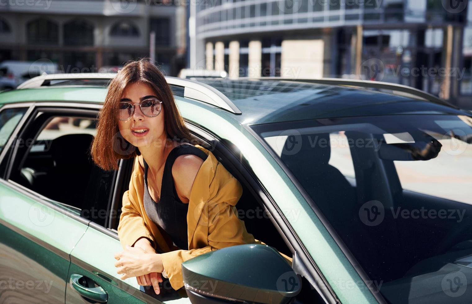 regarde de l'automobile. jeune femme à la mode en manteau de couleur bordeaux pendant la journée avec sa voiture photo