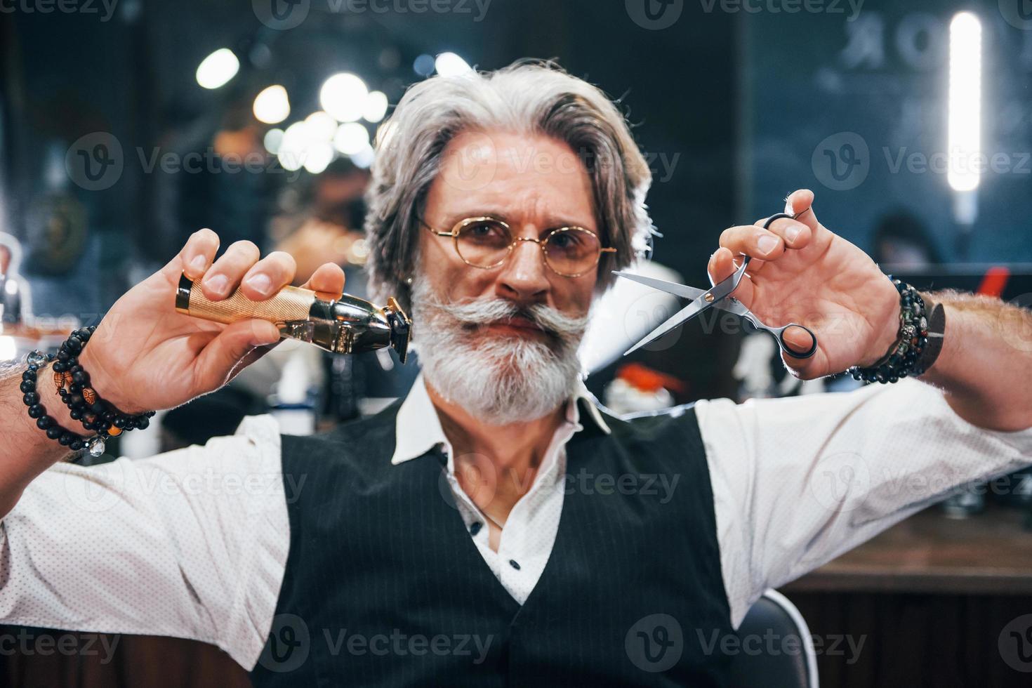 détient l'équipement de salon de coiffure. homme âgé moderne et élégant aux cheveux gris et à la barbe est à l'intérieur photo