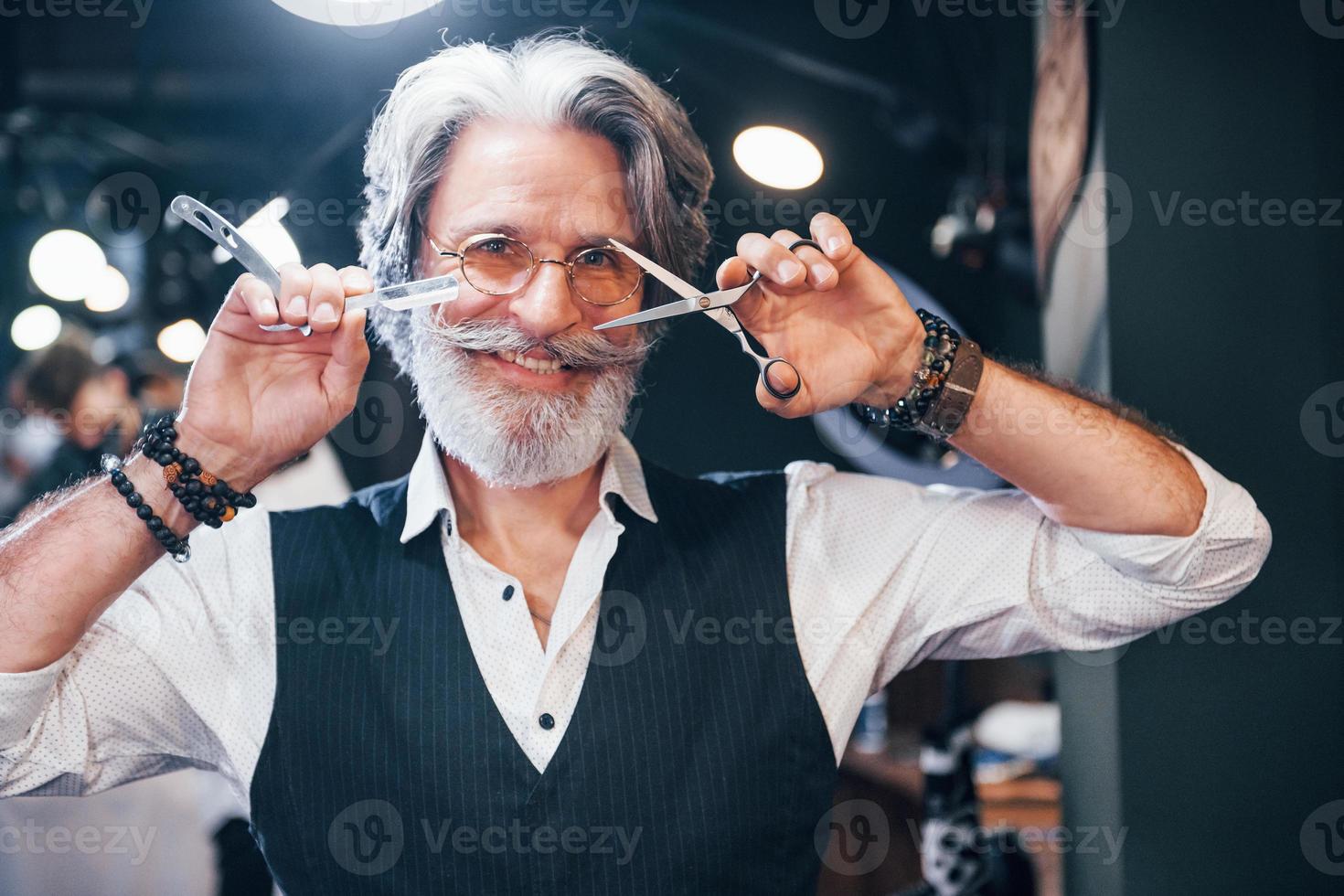 détient l'équipement de salon de coiffure. homme âgé moderne et élégant aux cheveux gris et à la barbe est à l'intérieur photo