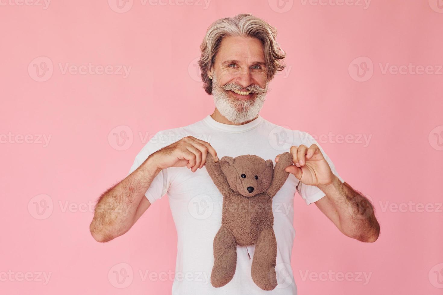 tient un ours en peluche. homme âgé moderne et élégant aux cheveux gris et à la barbe est à l'intérieur photo