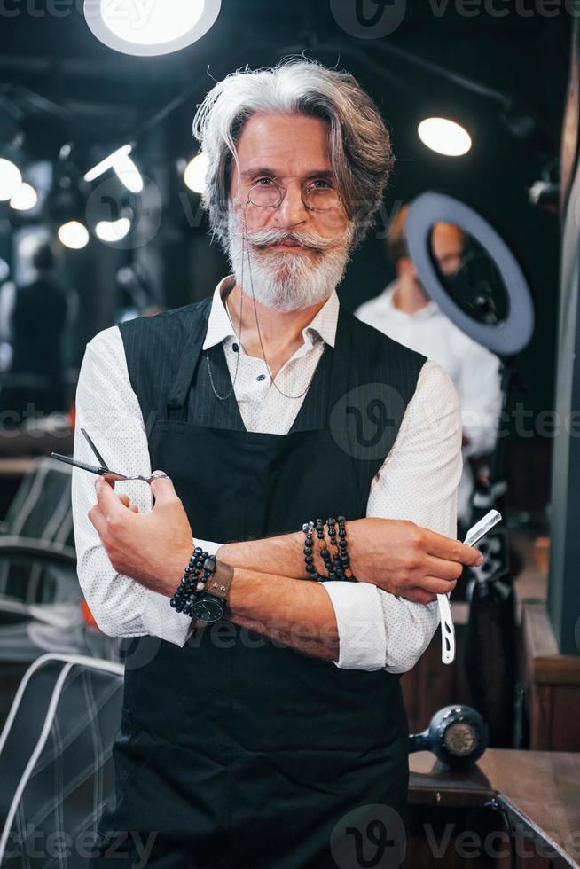 en salon de coiffure. homme âgé moderne et élégant aux cheveux gris et à la barbe est à l'intérieur photo