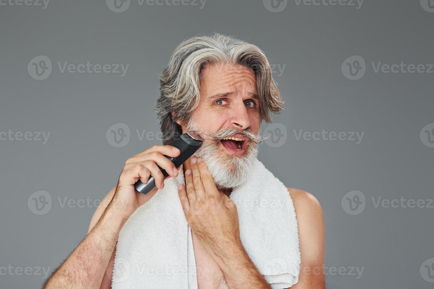 prendre soin de la barbe. homme âgé moderne et élégant aux cheveux gris est à l'intérieur photo