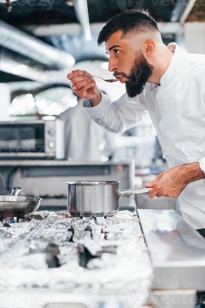 prépare une délicieuse soupe. chef en uniforme blanc cuisinant des aliments à la cuisine. journée bien remplie au travail photo