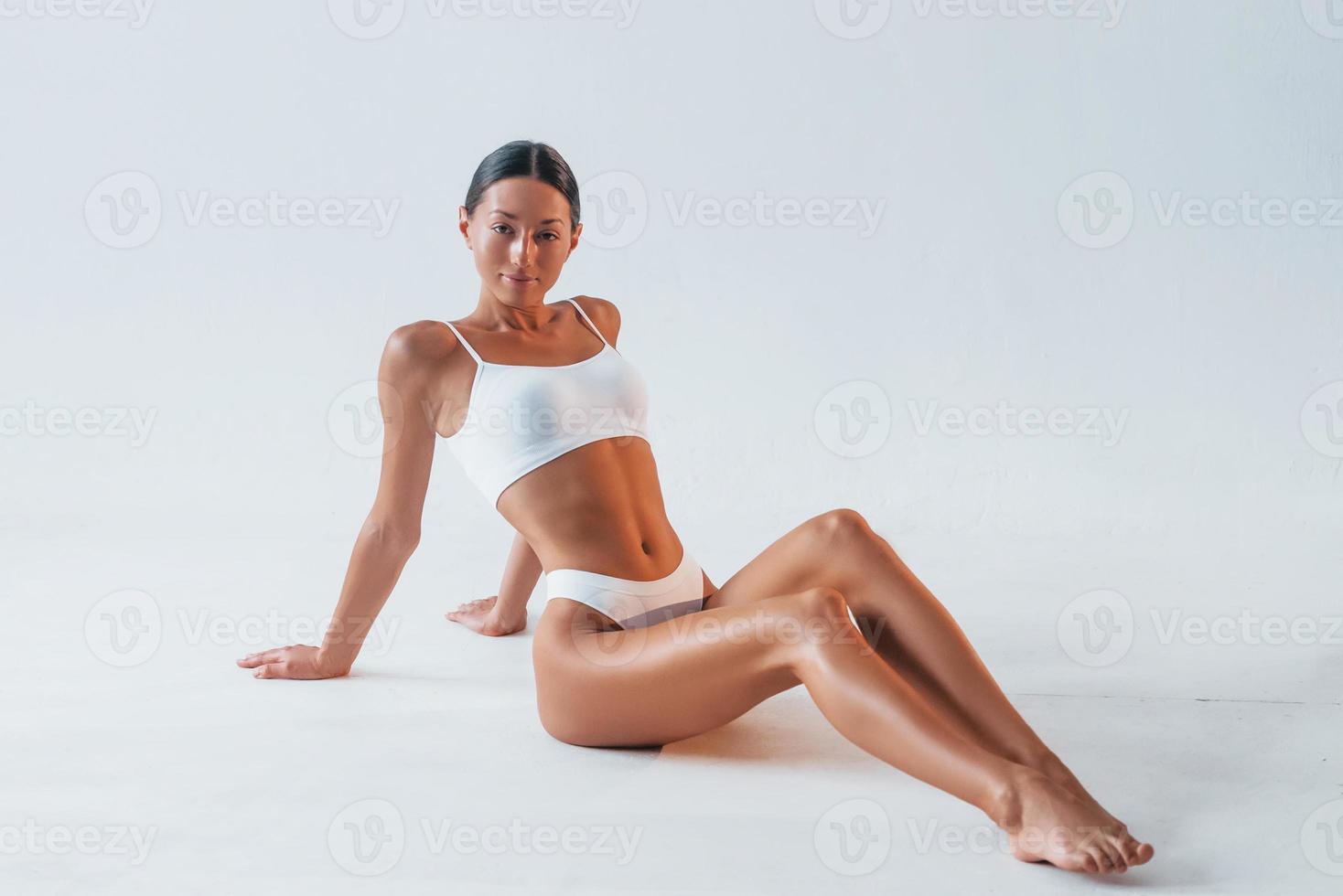 assis sur le sol. belle femme avec un corps mince en sous-vêtements est en studio photo