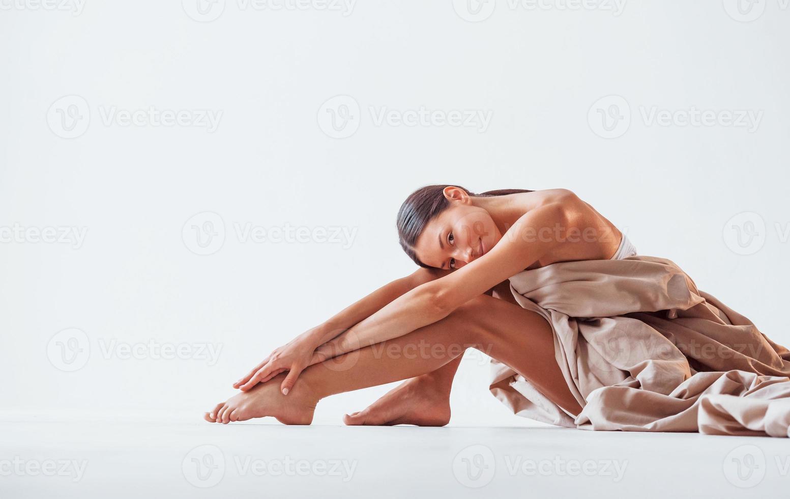 s'assoit et se couvre le corps d'un tissu. belle femme est en studio photo