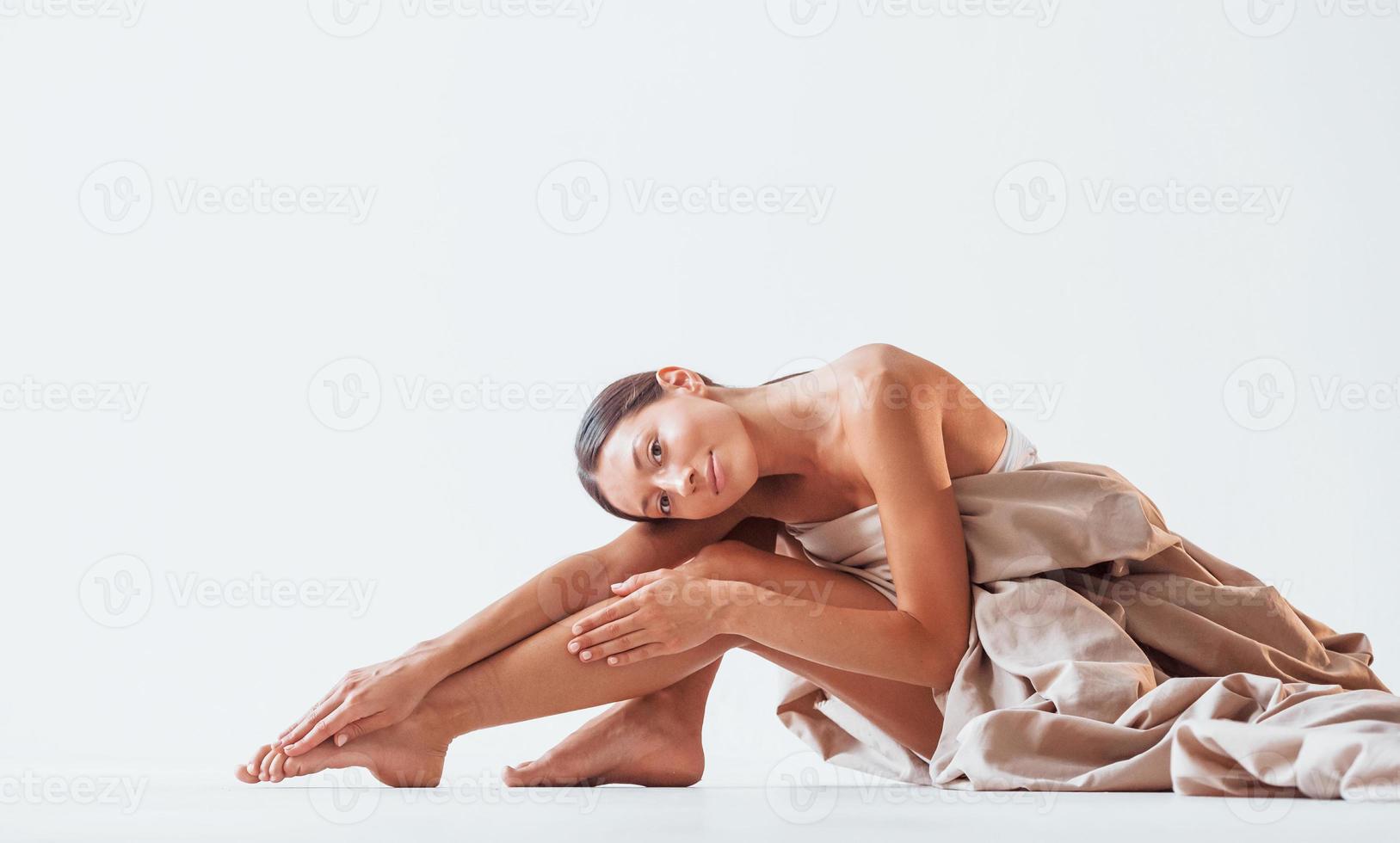 s'assoit et se couvre le corps d'un tissu. belle femme est en studio photo