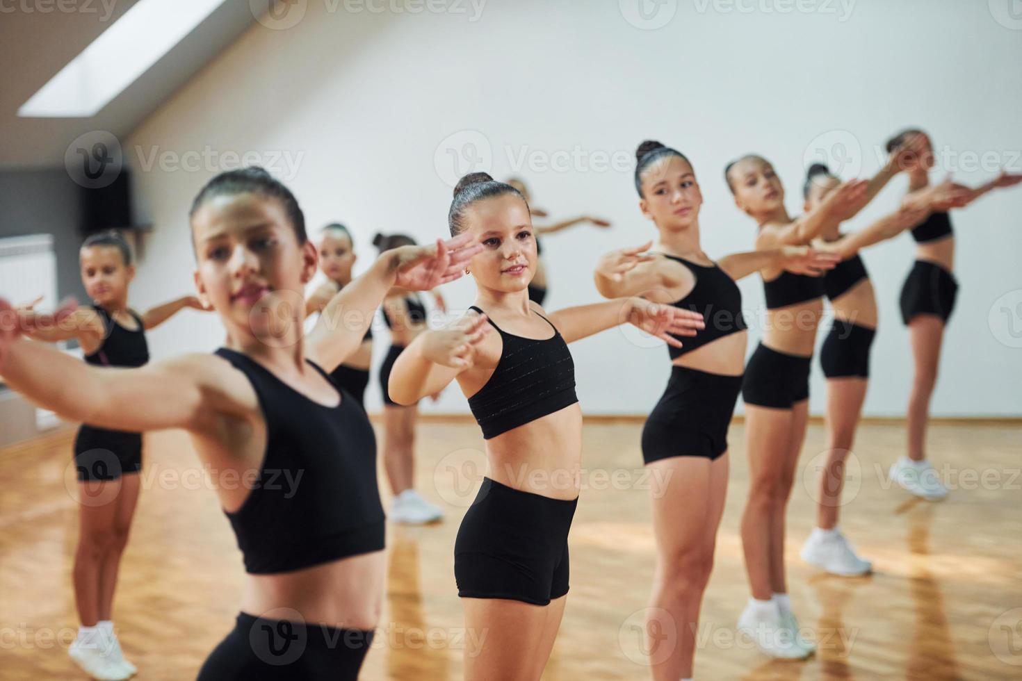 se tenir debout et faire des mouvements synchronisés. groupe d'enfants féminins pratiquant des exercices athlétiques ensemble à l'intérieur photo