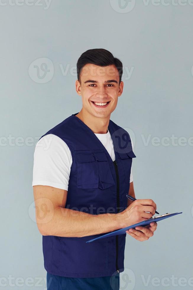 écrit dans le bloc-notes. travailleur masculin en uniforme bleu debout à l'intérieur du studio sur fond blanc photo