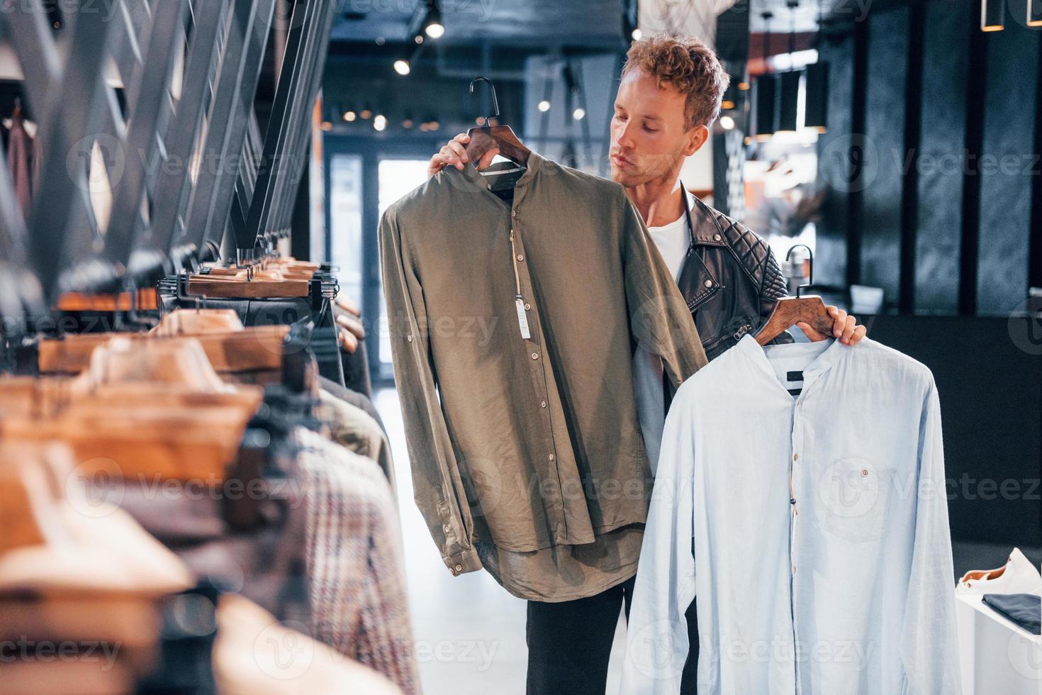 grand choix. jeune homme dans un magasin moderne avec de nouveaux vêtements. vêtements élégants et chers pour hommes photo