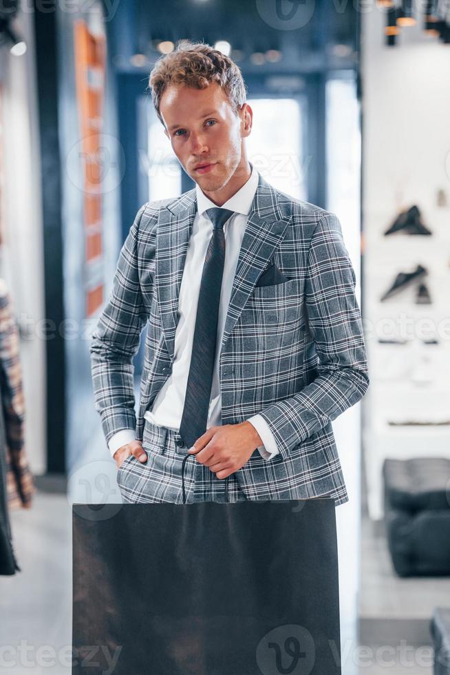 tient le sac avec l'achat. jeune homme dans un magasin moderne avec de nouveaux vêtements. vêtements élégants et chers pour hommes photo