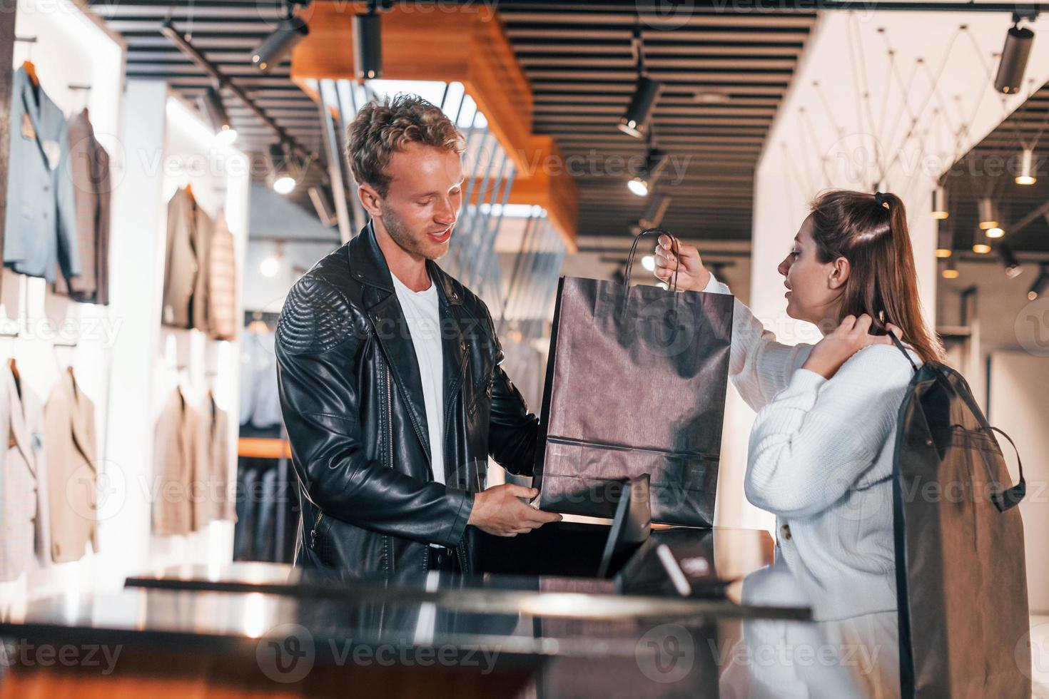 l'homme fait des achats dans un magasin moderne avec des vêtements élégants. une travailleuse sert le gars à la caisse photo