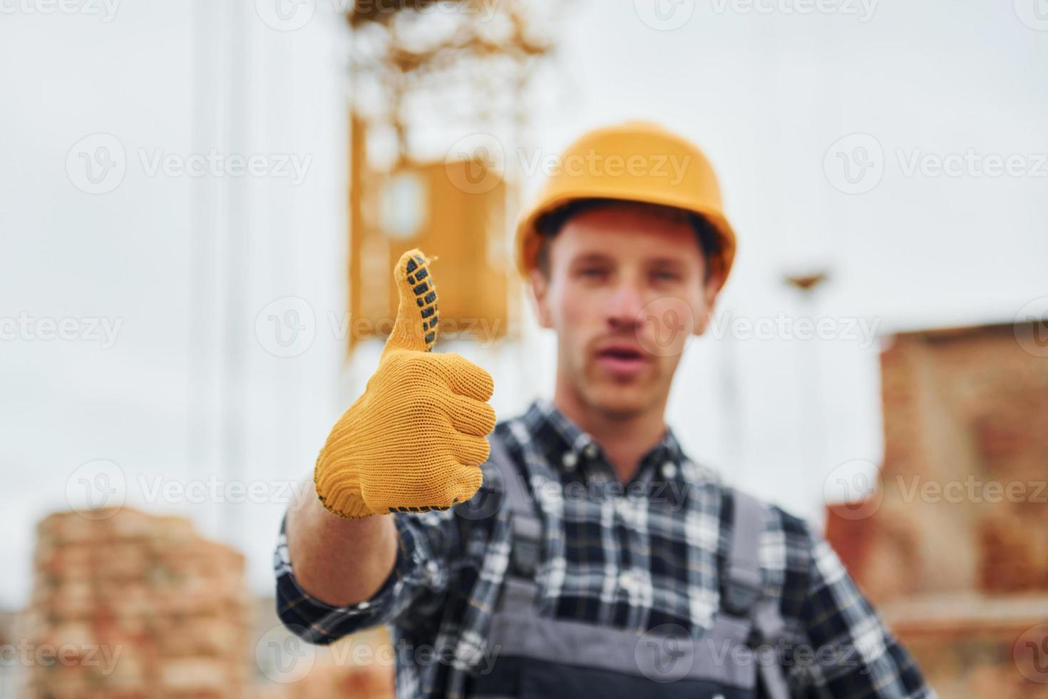 montre le pouce vers le haut. ouvrier du bâtiment en uniforme et équipement de sécurité a un travail sur le bâtiment photo